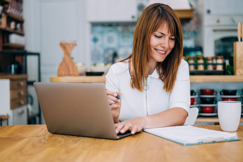 Frau sitzt neben einem Laptop und macht sich eine Checkliste